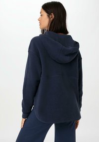 Dunkelblaues Fleece-Hoodie mit lockerer Passform, ausgestattet mit einer Kordelzugkapuze, langen Ärmeln und einem abgerundeten Saum. Weiche Textur erkennbar.