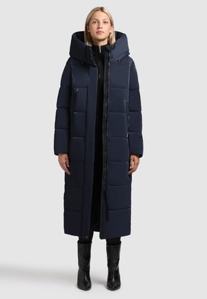 Lange navy pufferjas met hoge kraag, ritssluiting aan de voorkant, zijzakken en gestikt ontwerp. Zachte textuur en lichte isolatie.