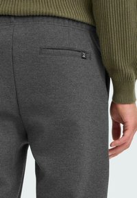 Szare, tkane spodnie o prostym kroju, wyposażone w tylną kieszeń i czarną metkę z logo. Tkanina ma teksturowany wygląd.