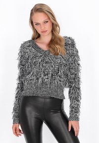 Fekete-fehér bolyhos kötött pulóver széles nyakkivágással és hosszú ujjaival, texturált rojtos mintázattal. Fekete leggings-szel viselve.