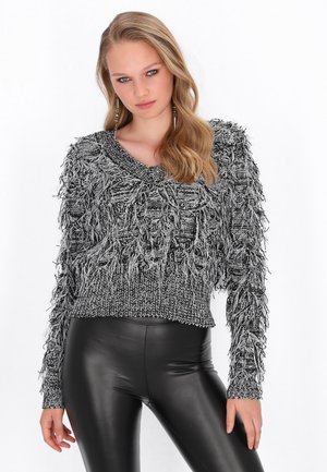Schwarzer und weißer, fuzzy Strickpullover mit weitem Ausschnitt und langen Ärmeln, der ein strukturiertes Fransen-Design aufweist. Getragen mit schwarzen Leggings.