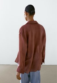 Lett, rustfarvet skjorte med en afslappet pasform, lange ærmer og klassisk krave. Blød tekstur med minimal detaljer.