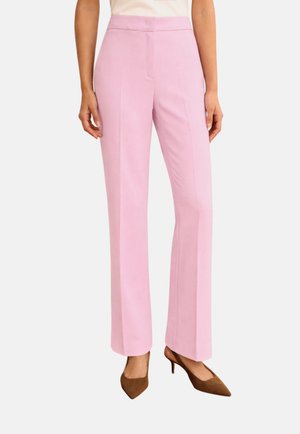 Donna che indossa pantaloni rosa pastello a vita alta e gamba dritta abbinati a décolleté marroni a punta e tacchi bassi, con top bianco infilato dentro.