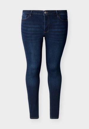 Jean skinny bleu foncé à cinq poches, bouton devant et fermeture éclair, présenté sur un fond blanc.