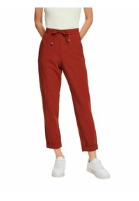 Czerwone spodnie dresowe z elastycznym pasem ze sznurkiem, podwiniętymi mankietami i bocznymi kieszeniami, wykonane z gładkiego materiału. W parze z białymi trampkami.