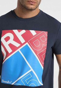 Navy blue cotton t-shirt featuring a large geometric print in red and blue with white text, short sleeves, and a round neckline.