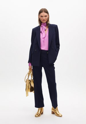Blazer navy con spalle decorate, blusa di satin rosa, pantaloni su misura, stivali oro alla caviglia e borsa metallica. Design semplice e strutturato.