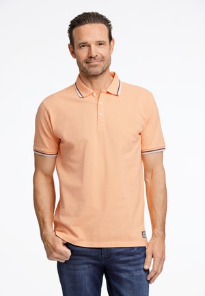 Polo shirt pêche avec un col, patte de boutonnage à trois boutons et accents rayés contrastants sur les manches. Porté avec un jean en denim foncé.
