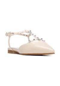 Zapatos planos beige con punta puntiaguda, con una estructura de tiras adornadas con tachuelas metálicas y un tacón bajo de color marrón claro.