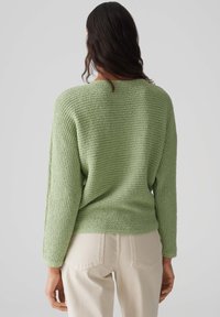 Grüner strukturierter Pullover mit lockerer Passform, langen Ärmeln und weitem Halsausschnitt, kombiniert mit hellen Jeans.