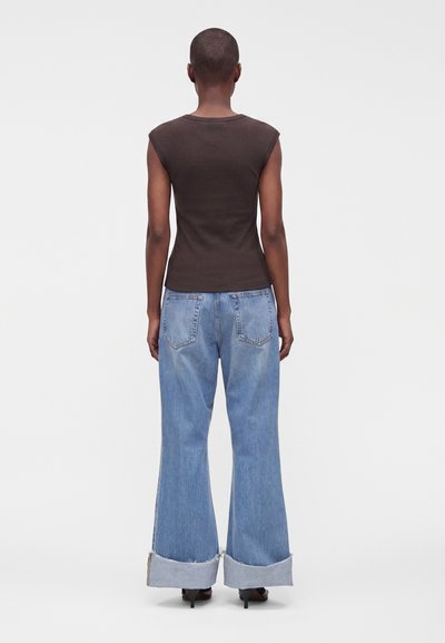 Femme vue de dos portant un haut sombre sans manches, un jean bleu clair à jambes larges avec de grands revers, et des sandales noires à talons hauts.
