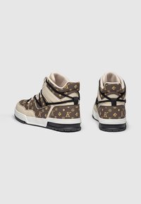 Zapatillas altas con un diseño en beige y marrón que presenta un patrón de logotipo repetido. Suela de goma negra, cuello acolchado y parte frontal con cordones.