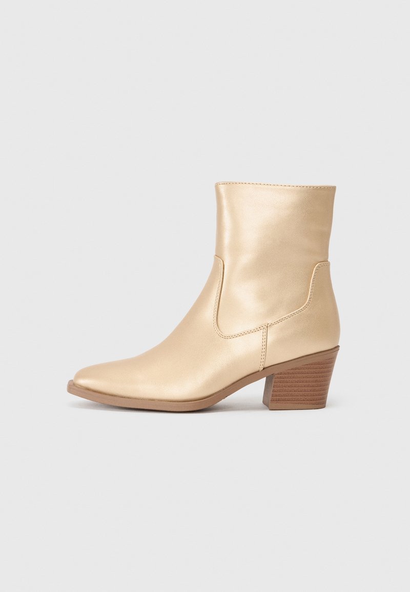 Bottine en cuir beige avec un bout pointu et un talon bloc empilé de hauteur moyenne, présentée sur un fond uni.