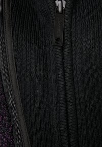 Chaqueta negra con cremallera que presenta una textura acanalada en el forro interior y un exterior liso con sutiles variaciones de color.