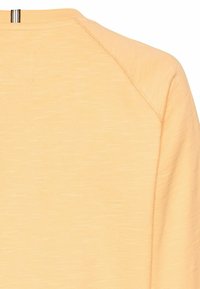 Lyse orange bomulds sweater med en tekstureret overflade. Den har en rund halsudskæring og raglanærmer med et lille lynlåselement på ryggen.