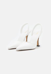 Bílé lakované slingback podpatky s špičatou špičkou, které mají tenký podpatek a černý akcent na podstavci. Hladká textura a minimalistický design.