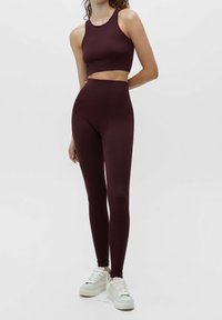 Ensemble de sport bordeaux comprenant un crop top ajusté avec un col rond et un legging taille haute, fabriqué en tissu extensible et lisse.