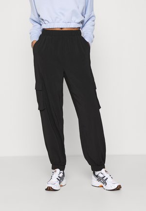 Person iført sorte cargo joggerbukser med elastiske manchetter og lommer, hvide sneakers og en lyseblå cropped sweatshirt.