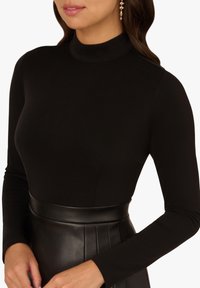 Schwarzes langärmeliges Oberteil mit Stehkragen aus glattem, elastischem Stoff, kombiniert mit einem hoch taillierten Lederrock mit Falten.