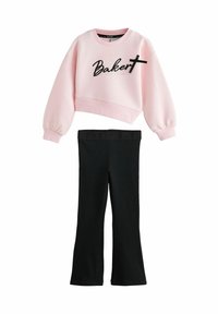 Felpa cropped rosa con la scritta "Baker" in nero corsivo e una croce, abbinata a leggings neri a campana. Tessuto morbido con vita elasticizzata.