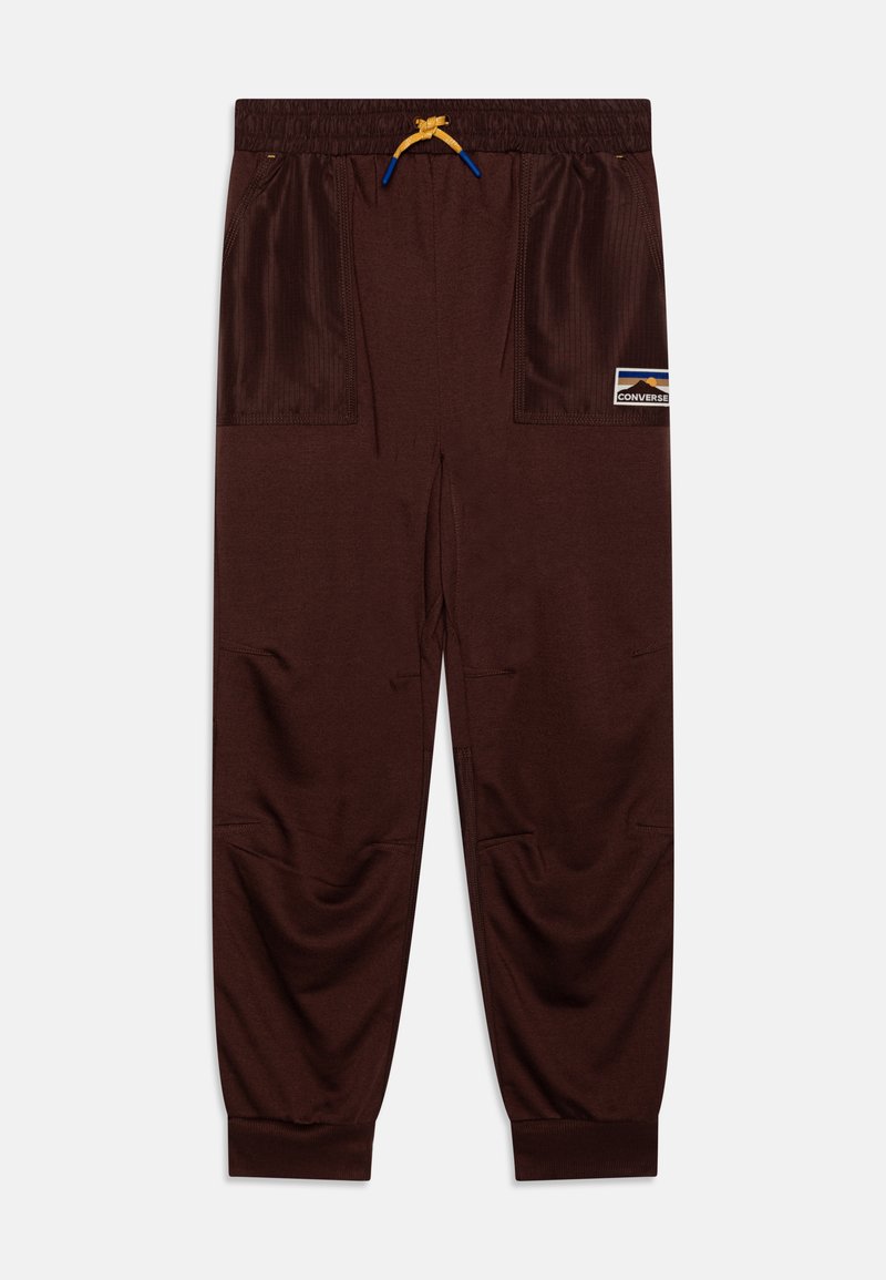 Bruine sportieve broek met een trekkoord in de taille, zijzakken, ribgebreide accenten en een patchlogo aan de linkerzijde. Glad textuur over de hele broek.