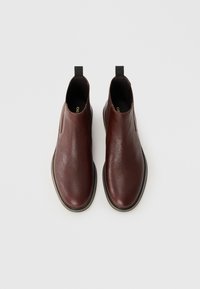 Bottines en cuir marron, avec un bout rond, présentant une surface texturée, une semelle contrastante et une petite languette à l'arrière pour un enfilage facile.