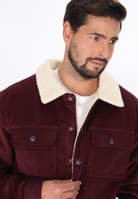 Burgunderfarvet fløjljakke med en beige shearling-krave, der har to brystlommer og sølvfarvede trykknapper. Blødt tekstur og skræddersyet pasform.