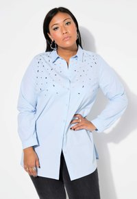 Camicia azzurro chiaro in cotone con maniche lunghe. Presenta borchie quadrate argentate sul davanti per un tocco di dettaglio in più.