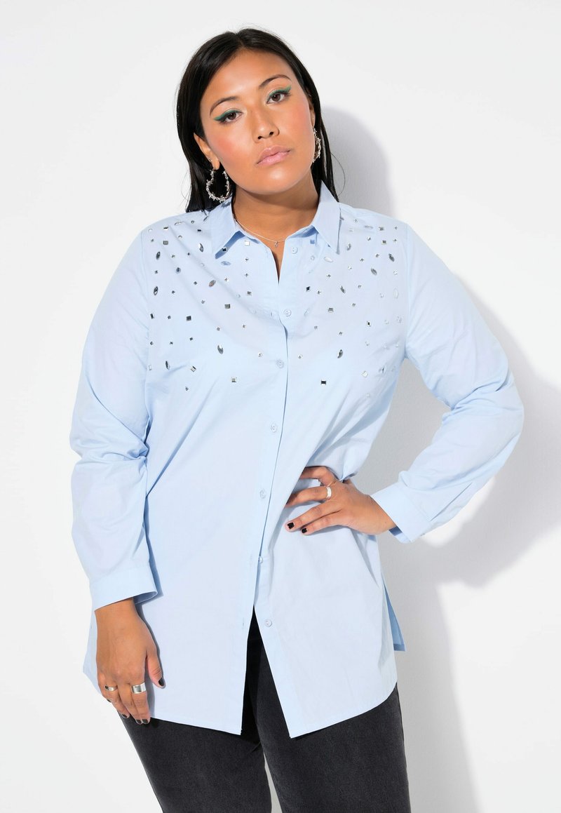 Camicia azzurro chiaro in cotone con maniche lunghe. Presenta borchie quadrate argentate sul davanti per un tocco di dettaglio in più.