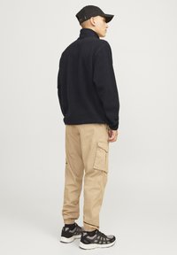 Sudadera negra de vellón con cuello alto, combinada con pantalones cargo beige con bolsillos laterales y zapatillas deportivas negras con detalles grises.
