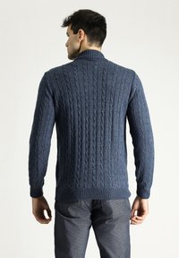 Dunkelblaues Strickpullover mit Ripptextur, verfügt über ein Kabelstrickdesign und einen hohen Kragen. Lange Ärmel und enganliegende Bündchen.