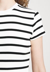 Czarna i biała koszulka w paski z krótkimi rękawami i okrągłym dekoltem. Materiał wydaje się miękki i dopasowany, z widocznym przeszyciem na rękawach.