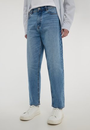 Jeans in denim azzurro chiaro con taglio dritto, caratterizzati da un classico design a cinque tasche e una leggera scoloritura. Abbinati a sneakers bianche.