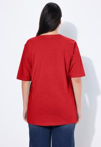 T-shirt rossa in cotone con una vestibilità comoda, maniche corte e scollo rotondo, vista da dietro su uno sfondo bianco uniforme.