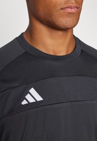 Svart träningsskjorta med korta ärmar, rund halsringning och en strukturerad panel över bröstet med en vit logotypdetalj.