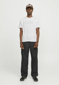 Hvid kortærmet t-shirt med grafisk tekst, parret med løstsiddende sorte cargo-bukser. En brun kasket med hvid tekst fuldender outfittet.