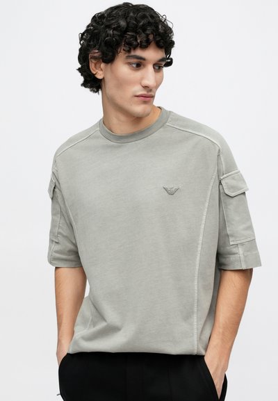 Svetlosivé tričko s krátkym rukávom a okrúhlym výstrihom, zdobené prešívaným detailom a malým logom na hrudi, vyrobené z mäkkej látky.