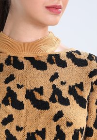 Luipaardprint trui in goudbeige met zwarte vlekken. Heeft een geribbelde, hoge halsontwerp en een zachte brei-textuur.