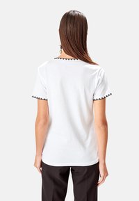 T-shirt bianco con bordo nero a scallop sul colletto e sulle maniche; maniche corte e vestibilità comoda; tessuto in cotone liscio e leggero.