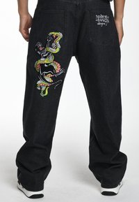 Zwarte denim broek met kleurrijke geborduurde ontwerpen van een slang en een panter op de achterkant. Loose fit met standaard zakken en stiksels.