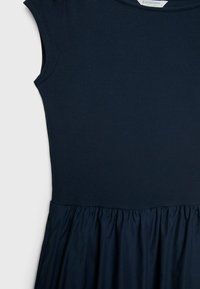 Marinblå klänning med ribbad textur upptill och en volangkjol. Bodicen har korta ärmar. Inga synliga mönster eller detaljer.