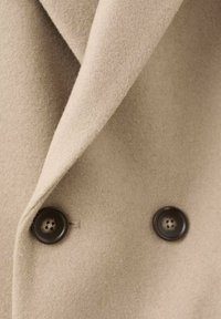 Tela de abrigo de mezcla de lana de color beige con una textura suave, que presenta un cuello de muesca y dos botones oscuros como acentos.
