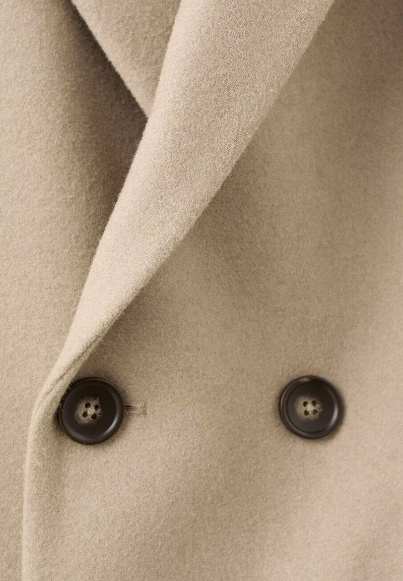 Beige wollen blend jasstof met een gladde textuur, voorzien van een notch revers en twee donkere knopen als accenten.