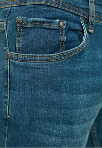 Jeans de mezclilla en azul oscuro con costuras naranjas, que presentan un bolsillo frontal y dos sólidos botones de metal. Textura suave con ligero desgaste.