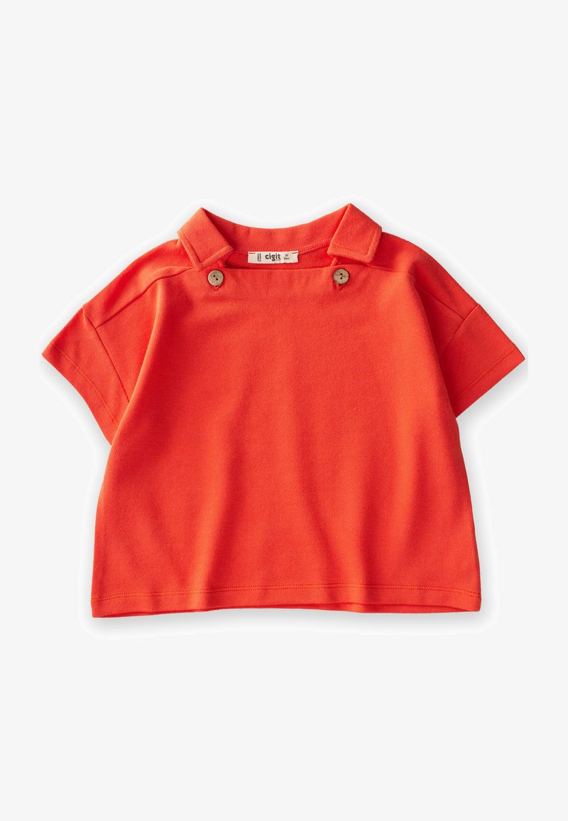 Trumpas rankovėmis oranžinis viršus, pagamintas iš medvilnės, su apykakle ir dviem dekoratyviniais mygtukais priekyje. Lygus paviršius ir kasdieniškas dizainas.