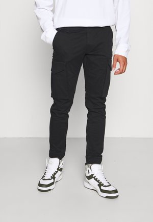 Zwarte cargobroek met een slim fit, voorzien van voor- en zijzakken, gemaakt van een duurzaam materiaal. Gecombineerd met wit en groen hoge sneakers.