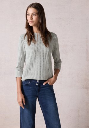 Hellgraues, strukturiertes Strickoberteil mit Dreiviertelärmeln, kombiniert mit blauen Jeans mit weitem Bein und Knopfdetails.