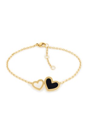 Bracelet chaîne en or avec deux pendentifs en forme de cœur reliés, l'un plein noir avec le texte "Hilfiger", l'autre un contour ouvert en or.