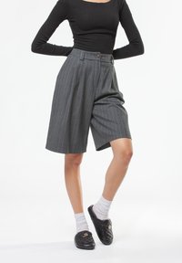 Shorts cintrés à fines rayures grises en tissu léger, avec taille haute, plis et fermeture par un seul bouton.