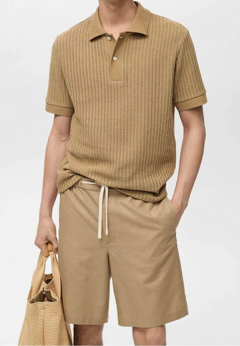 Homme portant un polo en maille beige et un short assorti, tenant un sac fourre-tout tissé beige dans une main, l’autre main dans la poche.
